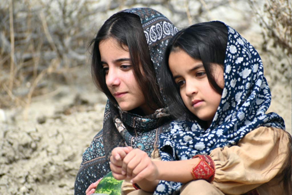 Two young girls with dark features wearing blue patterned head coverings.