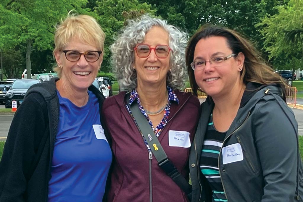 Three middle aged women wearing glasses smiling for the camera.