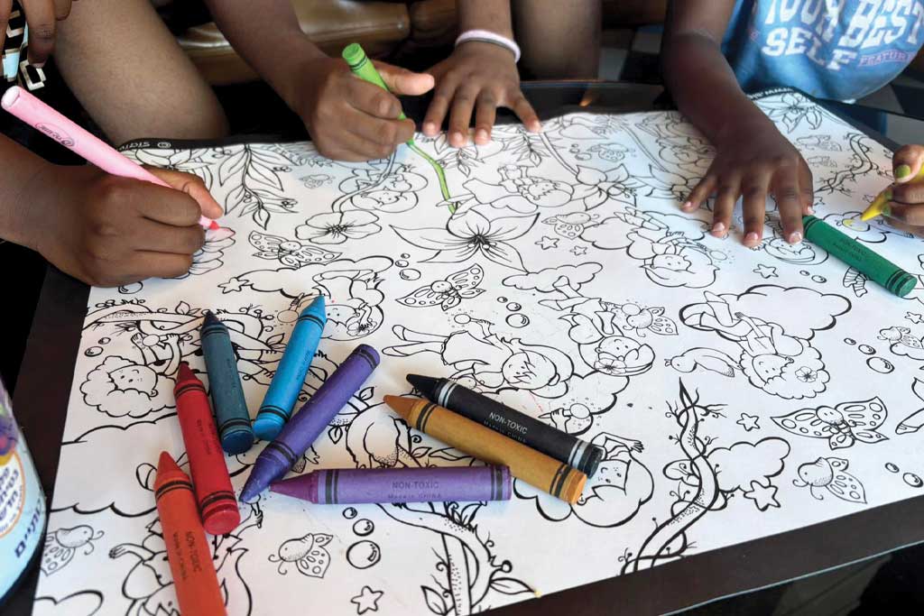 Crayons and kids coloring an open coloring book.