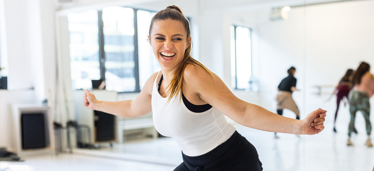 A young woman doing zumba wearing a white tank top with a high ponytail.