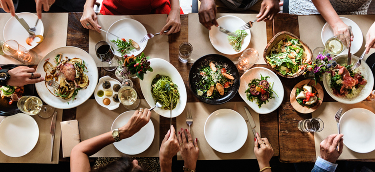 Overview of a dinner table filled with plates and hands passing food.