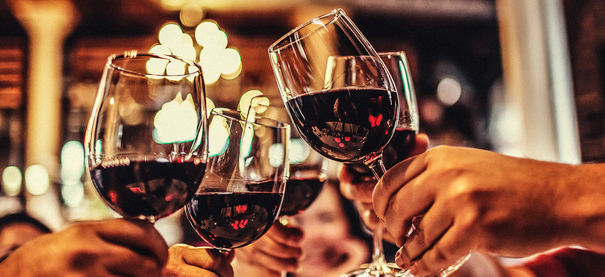 Red wine in clear wine stem glasses clinking in cheers.