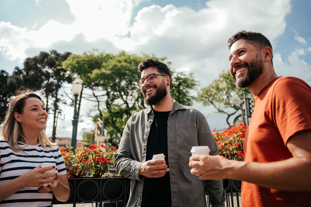 Two men and one woman holding coffee cups outside chatting