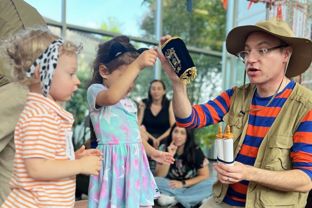 An image of an man and children holding a little Torah